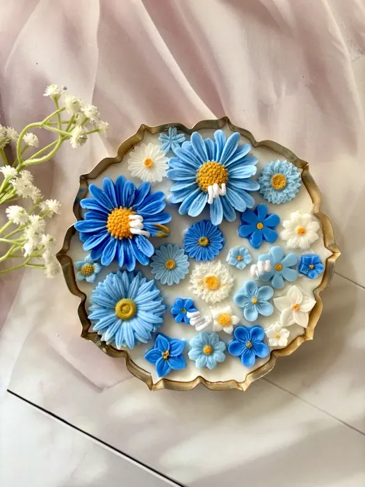 A gold-rimmed tray packed with sculpted blue cornflowers, daisies and forget-me-nots, on pale pink tulle.